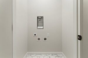 A small, white entryway with hexagonal tile flooring, featuring a thermostat and various wall switches.