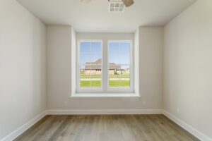 An empty room with light wooden floors and a large bay window showing a suburban view.