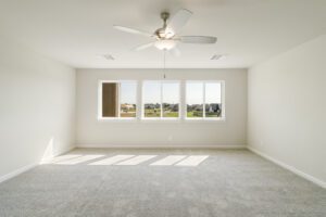 Empty room with carpeting, ceiling fan, and a large window showing a suburban view.