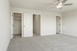 Empty modern bedroom with carpet, featuring two open closet doors and a ceiling fan.
