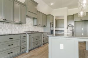 Modern kitchen with sage green cabinets, white hexagonal tile backsplash, and stainless steel appliances.