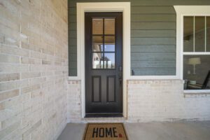 A welcoming entrance showcasing a modern front door with glass panes, flanked by cream brick and green siding, complete with a welcoming doormat that reads "home.