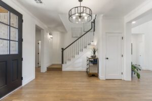 Modern and spacious entryway with a stylish staircase, elegant lighting, and clean, white walls complemented by dark trim and hardwood floors.