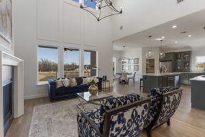 Spacious modern living room connected to a kitchen with high ceilings, large windows, and contemporary furniture with bold blue accents.