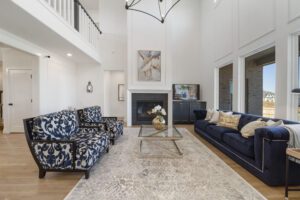 Spacious living room with high ceilings, featuring a white fireplace, navy blue sofas, patterned chairs, and a glass coffee table on a large area rug.