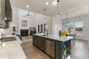 Modern kitchen with a central island, pendant lights, and a view of a living room with a fireplace. bright, spacious interior with high ceilings and hardwood floors.