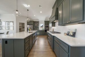 Modern kitchen interior with gray cabinetry, white countertops, hardwood floors, and pendant lighting.
