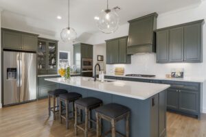 Modern kitchen with dark green cabinets, stainless steel appliances, and a central island with bar stools.