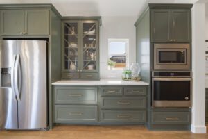 Modern kitchen with sage green cabinetry and stainless steel appliances.