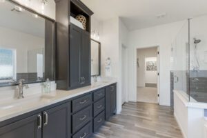 Modern bathroom featuring dual sinks with dark cabinetry, a well-lit vanity area, a walk-in shower with glass doors, and elegant tile flooring, exuding a sleek and contemporary design.