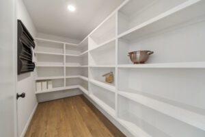 A walk-in closet with empty white shelves and a single decorative bowl on a shelf.