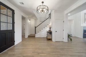 A spacious, modern entryway with hardwood floors, a staircase, white walls, and black accent doors.