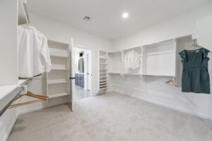 Spacious walk-in closet with white shelving, hanging clothes, and carpeted floors in a modern home.