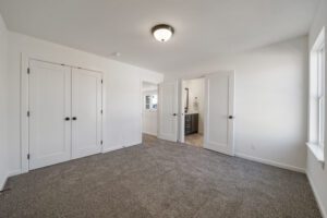 Empty room with gray carpet, white walls, and three closed white doors.