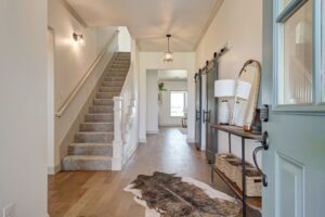 A modern hallway with a staircase on the left and a console table with a lamp on the right. A sliding barn door leads to another room. A cowhide rug is on the wooden floor.