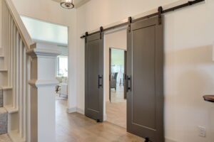 A hallway featuring sliding barn doors, light wood flooring, and a staircase with white railings leading to a bright living room.