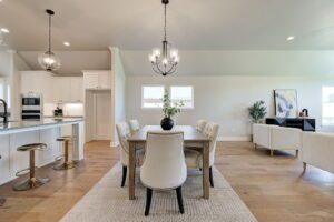 Open-concept dining and living area with a large table, upholstered chairs, a chandelier, a kitchen island with bar stools, and modern decor on hardwood floors.