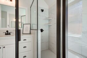 Modern bathroom with glass shower door, white cabinetry, black fixtures, and a decorative frame on the countertop.