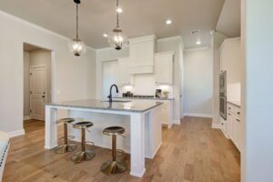 Modern kitchen with a large island, granite countertop, and three stools. Pendant lights above the island and white cabinets create a sleek and bright appearance.