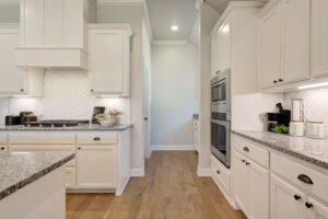 Modern kitchen with white cabinets, granite countertops, stainless steel appliances, and wood flooring.