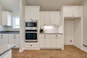 A modern kitchen with white cabinets, a double oven, granite countertops, and hardwood floors.